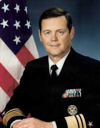 Formal portrait of U.S. Navy Vice Admiral Thomas R. Wilson in uniform standing in front of the American flag
