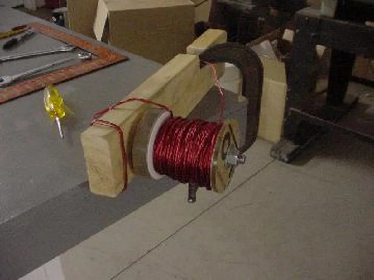 A Tesla coil setup showing a wooden structure with red wire wound around a spool