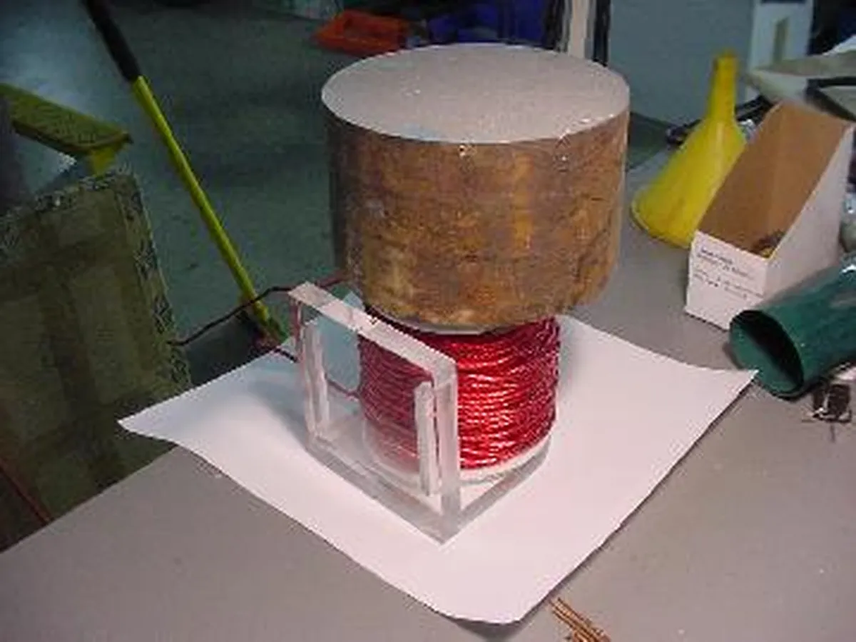 A close-up view of a Tesla-style glue coil device featuring a red wire coil and a wooden cylinder on top